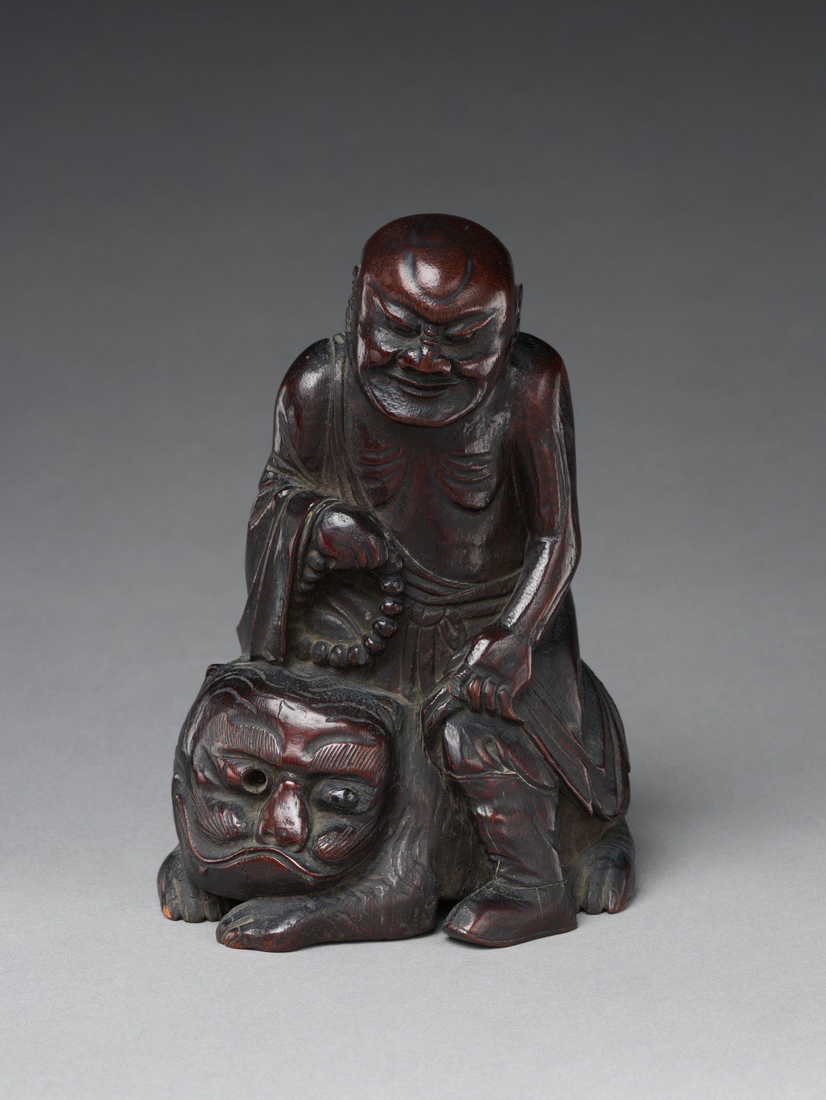 Holz-Netsuke, das eine lachende Buddha-Figur mit einem Affen auf einem weißen Hintergrund zeigt.