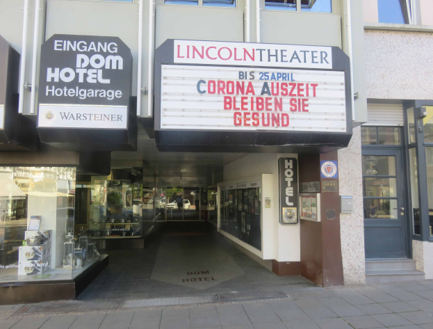 Außenansicht des Lincoln Theaters in Berlin, Deutschland, mit Glasfenstern, Türen und einer Texttafel, sowie einer belebten Stadtlandschaft im Inneren.