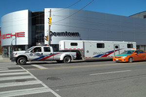 Ein Polizeifahrzeug vor einem Gebäude mit Text geparkt, eine Verkehrsampel mit einem Mast und Drähten im Vordergrund und Bäume mit einem klaren blauen Himmel im Hintergrund.